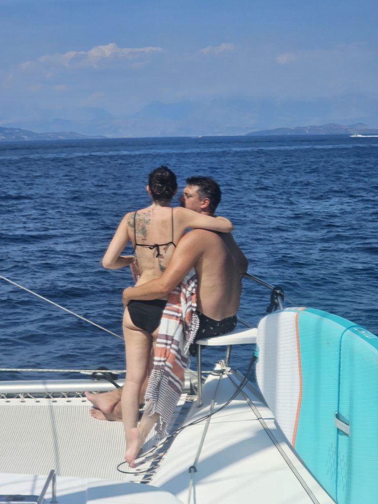 couple enlacé à l'avant du catamaran, la femme regarde la mer et l'horizon